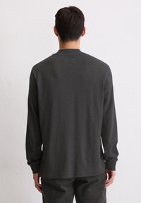 Długorękawowa ciemnoszara koszula z zaokrąglonym dekoltem, miękką teksturą i luźnym krojem. Charakteryzuje się prostym wzorem bez widocznych logo.