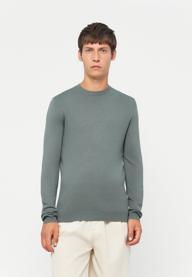 Light gray long-sleeve sweater made of a smooth knit fabric, featuring a round neckline and ribbed cuffs. Simple, fitted design.