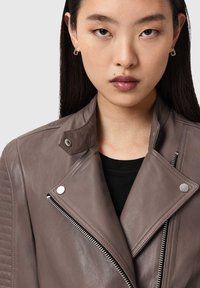 Braune Leder-Motorradjacke mit gesteppter Schulterpartie, einem Reverskragen, silbernen Reißverschlüssen und Druckknöpfen; darunter ein schwarzes Oberteil kombiniert.