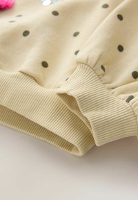 Lys beige sweatshirt med mørkegrønne prikker. Ribbet manchetter og kant, med en blød stofstruktur. Dekorative detaljer synlige.