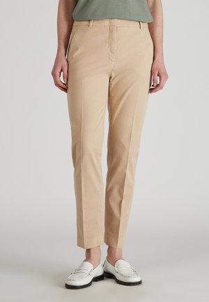 Beige Baumwollhosen mit gerader Passform, die über eine glatte Struktur, Fronttaschen und einen mittelhohen Bund verfügen. Kombiniert mit weißen Slippern.