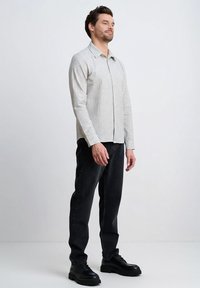 Jasnoszara koszula w kratę na guziki z ostrym kołnierzykiem, noszona z czarnymi dżinsami i masywnymi czarnymi butami, prezentująca luźny krój i gładką fakturę.