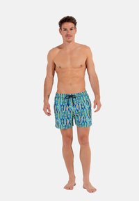 Maillot de bain à motifs bleus et verts avec une taille à cordon, présentant un design de planche de surf et fabriqué dans un tissu léger et à séchage rapide.