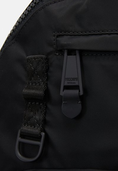 Rucsac din nylon negru cu o suprafață texturată, curea ajustabilă și un fermoar personalizat cu inscripția "Moschino Milano".