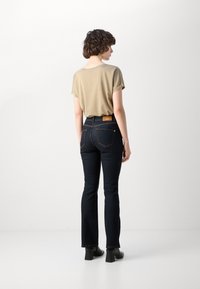 Guld t-shirt med kort ärm och uppvikta ärmar, kombinerad med mörkblå utsvängda jeans som har en läderlapp på baksidan och kontrasterande sömmar.