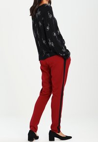 Zwarte blouse met lange mouwen en bloemenprint, gecombineerd met rode getailleerde broek met zwarte zijkanten. Aangevuld met zwarte blokhakken.