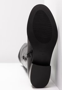 Schwarzer, strukturierter Stiefel mit Reißverschluss, Sohle sichtbar mit Profilmustern und Größenmarkierung 4, vor einem weißen Hintergrund positioniert.