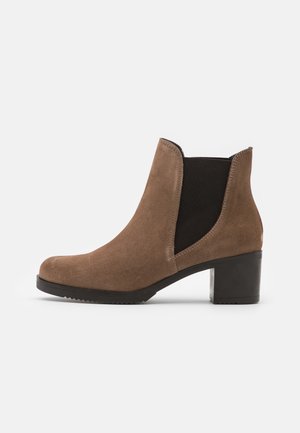 Bottine en suede marron avec une empeigne élastique noire sur le côté, bout rond et talon empilé. Semelle texturée pour une meilleure adhérence et stabilité.