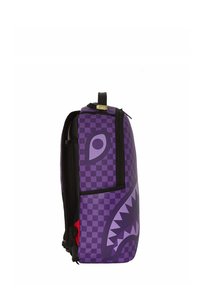 Zaino viola con motivo a scacchi, un design di un volto mostruoso prominente e una finitura testurizzata. Include una tasca laterale e accenti neri.