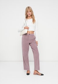 Lichtpaarse corduroy wijde broek met hoge taille, gecombineerd met een witte blouse met lange mouwen en een beige handtas, gedragen met zwart en naaktkleurige platte schoenen.