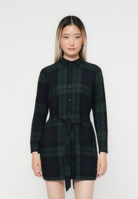 Robe chemise ajustée à carreaux en vert foncé et bleu marine, avec un devant boutonné, des manches longues, un col et une ceinture à la taille pour un ajustement réglable.