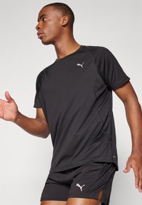 Schwarzes Sport-T-Shirt mit kurzen Ärmeln, gefertigt aus leichtem Material. Verfügt über ein kleines weißes Logo auf der Brust und eine glatte Textur.