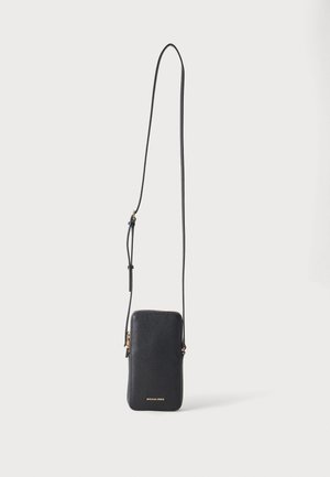 Sac téléphone bandoulière en cuir noir texturé avec une longue sangle réglable et une fermeture éclair dorée, logo Michael Kors en petites lettres dorées en bas.