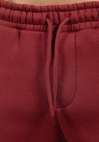 Bordeaux joggingbroek met een elastische tailleband en verstelbaar trekkoord. Glad oppervlak met zijzakken en een getailleerd ontwerp.