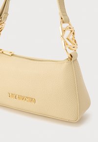 Μπεζ δερμάτινη τσάντα με υφή, σε τριγωνικό σχήμα, με χρυσαφί μεταλλικά στοιχεία και κλείσιμο με φερμουάρ. Διαθέτει το λογότυπο "LOVE MOSCHINO" σε χρυσά γράμματα.