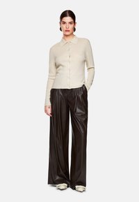 Helle beige gestrickte Strickjacke mit einem Kragen und knöpfbarem Front, kombiniert mit hoch-taillierten, weiten braunen Lederhosen.