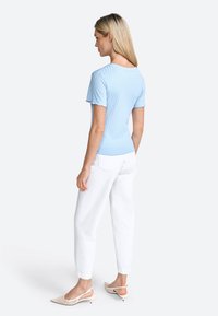 Lyseblå ribbet top med korte ærmer, der har en rund halsudskæring og rynkede kanter, parret med hvide løse bukser og beige slingback- hæle.