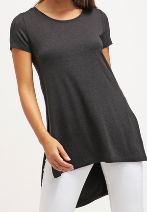 Tunic corta nera a maniche corte in un tessuto morbido, con scollo rotondo e orlo posteriore più lungo, abbinata a jeans skinny bianchi.