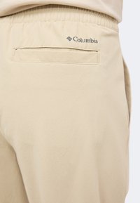 Οπίσθια όψη μπεζ παντελονιών Columbia με ελαστική μέση και μία μονή τσέπη με επένδυση στη δεξιά πλευρά.