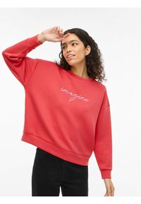 Czerwona bluza z luźnym krojem, okrągłym dekoltem i długimi rękawami. Na przodzie wyszyte słowo "imagine" w kontrastowym kolorze.