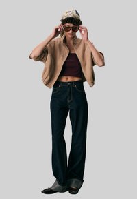 Khaki kordfløjl bomberjakke, tilpasset maroon crop top, lige ben mørke jeans og sorte sko med grå accenter; accessorized med solbriller.