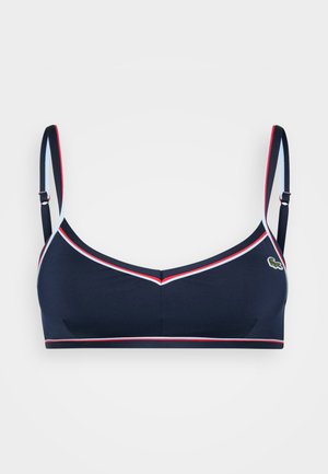 Reggiseno sportivo blu navy con bordi bianchi e rossi, spalline regolabili e un piccolo logo decorativo. Tessuto liscio con un taglio semplice.