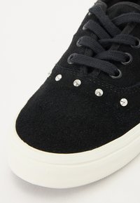 Black suede sneaker with silver studs along the upper, round toe, and white rubber sole. Features flat black laces and smooth texture.