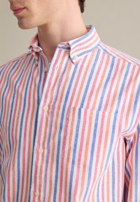 Camisa de botones con rayas verticales en rojo, rosa y azul. Fabricada con un tejido ligero, con cuello y bolsillo en el pecho izquierdo.