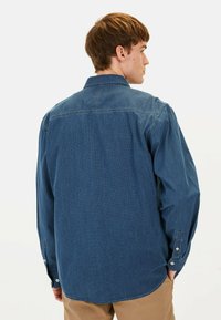 Denimhemd in tiefblau mit einem subtilen Texturmuster, langen Ärmeln, Knopfmanschetten und einem klassischen Kragen, von hinten gezeigt.
