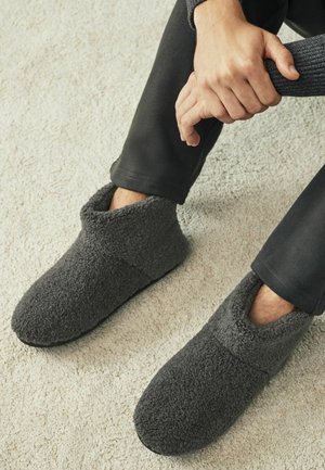 Graue Fleece-Hausschuhe mit Knöchelhöhe und einem weichen, strukturierten Äußeren. Sie haben eine runde Zehenpartie und einen niedrigen Schnitt für ein einfaches Anziehen.