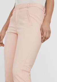 Růžové kalhoty na míru s hladkým povrchem, úzkým střihem, bočními kapsami a jemnými švy na bocích.