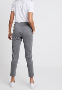 Grå avsmalnande byxor med elastisk midja, tillverkade av ett mjukt tyg. Kombinerat med en vit skjorta och vita sneakers, sedd bakifrån.