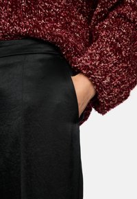 Textured burgundy knitted sweater with flecks, paired with smooth black pants featuring side pockets and a fitted waistband.