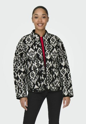 Gepolsterte Jacke mit einem schwarz-weißen geometrischen Muster, mit Stehkragen und Fronttaschen, getragen über einem roten Oberteil.