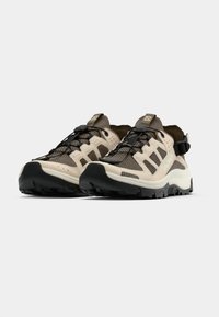 Chaussures de randonnée avec une tige en mesh beige léger, une semelle en caoutchouc marron et des accents noirs. Comprend des sangles de talon réglables pour un maintien sécurisé.