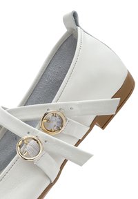 Scarpa bianca in pelle con cinturini incrociati, anelli dorati e suola in gomma marrone chiaro. Caratterizzata da una punta arrotondata e una texture liscia.