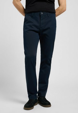 Chinos azul marino hechos de una mezcla de algodón, con un diseño de pierna recta, bolsillos delanteros y cierre de botón. Combinados con zapatillas negras.
