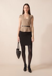 Béžový peplum top s krátkými rukávy v kombinaci s černou přiléhavou tužkovou sukní. Černé neprůhledné punčocháče a lodičky se špičkou. Nese černou kabelku.