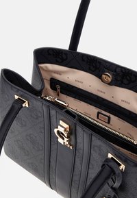 Borsa tote nera Guess con chiusura logo dorato, manici doppi, fodera interna beige con marchio Guess e tasca interna con zip.