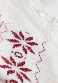 Kreminės spalvos megztinis su raudonais blizgančiais snaigės ir geometriniais raštais. Minkštos tekstūros su briaunotu kaklu ir rankogaliais.