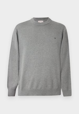 Világosszürke, környakú pulóver kötött anyagból. Rugalmas mandzsettákkal és aljjal rendelkezik, a bal mellen pedig egy kis fekete logó található.