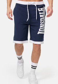 Navy blue shorts with white trim and a bold "TONSDALE" print on the side. Features drawstring waist and two side pockets.
