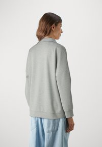 Sudadera gris de gran tamaño con cuello, puños de canalé, textura suave y un ajuste relajado, combinada con jeans de pierna ancha de color azul claro.