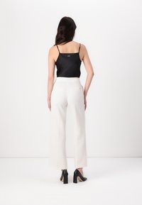 Musta satiinikangas camisole ohuilla olkaimilla, yhdistetty valkoisiin leveälahkeisiin housuihin ja mustiin korkeakorkoisiin kenkiin. Minimalistinen muotoilu puhtailla linjoilla.