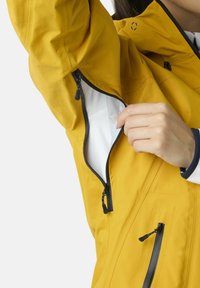 Giacca impermeabile gialla con zip nere, che mette in evidenza una tasca laterale. Il materiale appare liscio con un design leggero e flessibile.