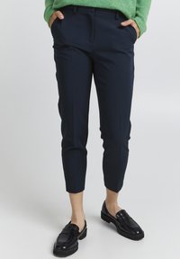 Granatowe spodenki z taliowaniem, slim fit, w krótkiej długości, z przodem z wyprasowaniem i bocznymi kieszeniami, zestawione z czarnymi loafersami. Miękka tekstura.