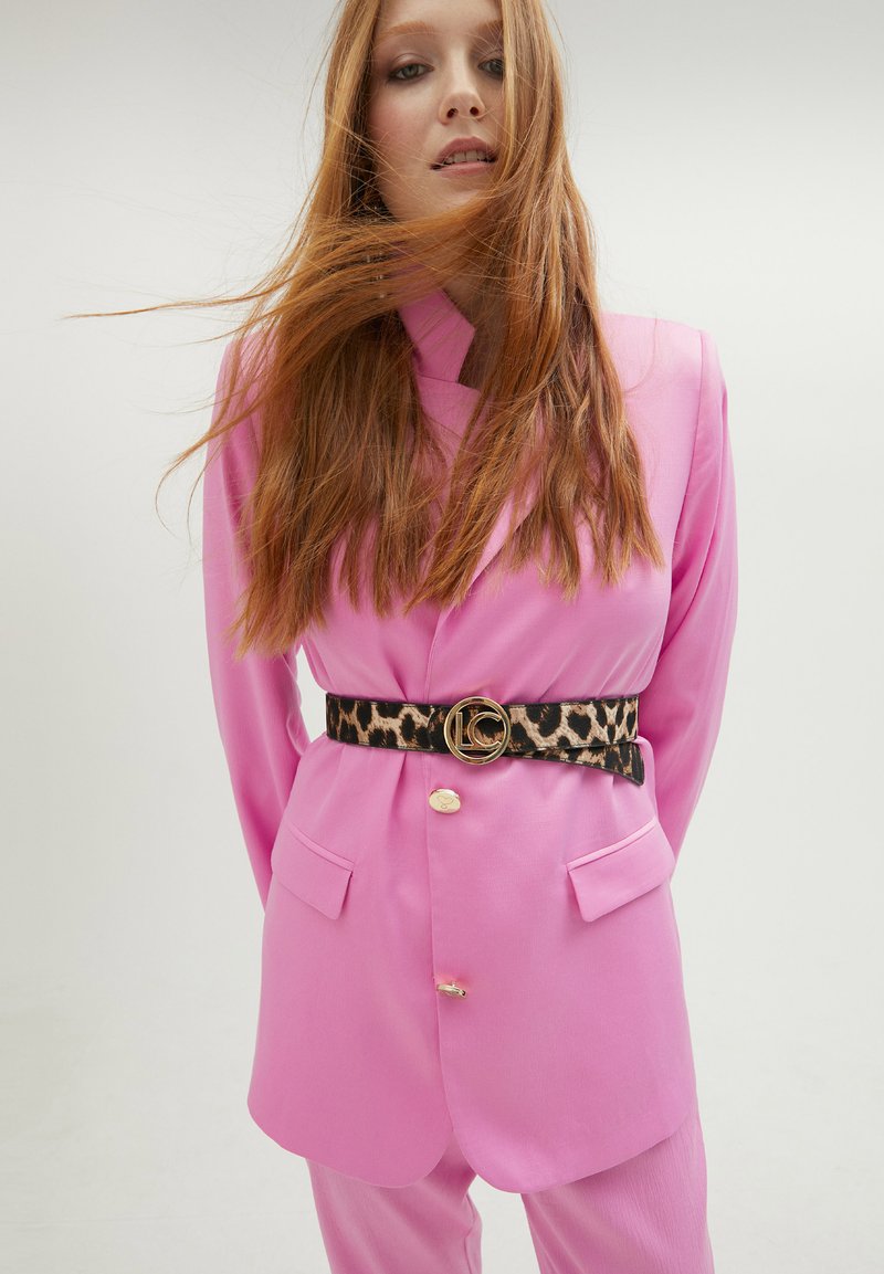 Rosa skräddarsydd kavaj med dubbelknappning och framfickor, ihop med ett leopardmönstrat bälte med en gyllene rund spänne.