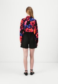 Blomstermønstret bluse i sterke farger, sammen med svarte shorts. Blusen har lange ermer og krage; shortsen har elastisk liv.
