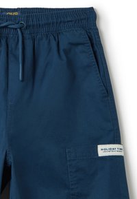 Bermudas azul marino con cintura elástica y cordón. Presenta un bolsillo lateral y una etiqueta que dice "HOLIDAY TIME". Textura suave.