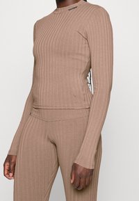 Brązowa prążkowana bluzka z długim rękawem, okrągłym dekoltem i rozcięciami po bokach, w połączeniu z dopasowanymi prążkowanymi legginsami, prezentująca elastyczną tkaninę i dopasowany krój.